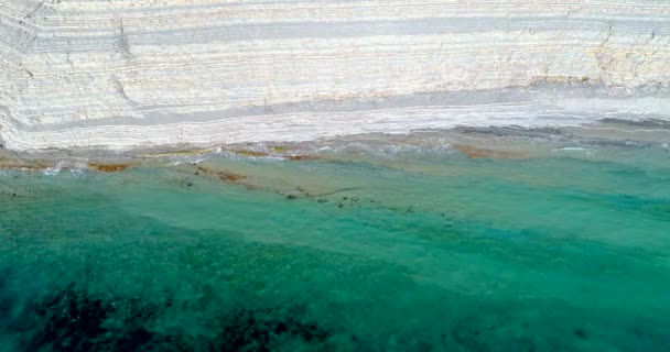 Полет над побережьем Черного моря под Геленджиком. Берег с высокими белыми скалами слоистой структуры. На скалах - лес. На побережье есть узкий галечный пляж. Гладкое голубое прозрачное море — стоковое видео