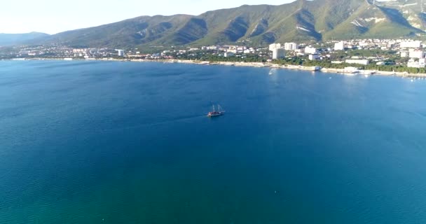 Gledesskipet går langs Gelendzhik-bukta og nærmer seg Gelendzjiks sentrale kaiplass. Kaukasus-fjellene er i bakgrunnen. Blått vann i bukta. En stor vannforekomst med en – stockvideo