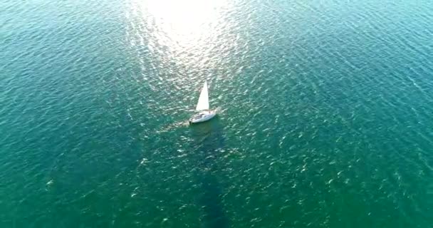 Turkuaz denizde yelkenli altında bir yat. Batan güneş yelkenden gelen suyun üzerinde uzun bir gölge bırakır. — Stok video