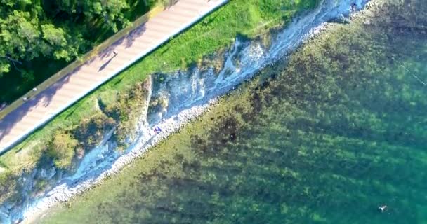 Flug über den Strand des Ferienortes Gelendzhik im Sommer. Kiesstrand, Böschung mit Fliesen, Balustrade. Es gibt Liegestühle und Strohschirme am Strand. Felsbrocken der Buhnen. Menschen schwimmen — Stockvideo