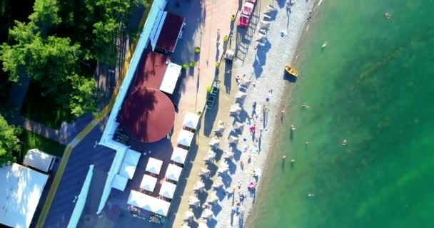 Vlucht over het strand van Gelendzhik resort in de zomer. Kiezelstrand, dijk met tegels, balustrade. Op het strand staan ligbedden en stroparasols. Boulders van de golfbrekers. Mensen zwemmen. — Stockvideo