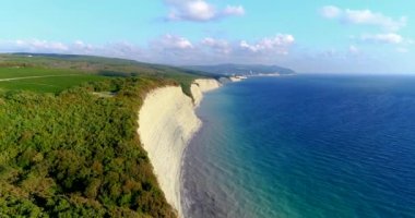 Büyük beyaz kayalarla Karadeniz kıyısında uçuyorlar. Kayaların dibinde küçük bir çakıl taşı plajı var. Ormanın kıyısında. Arka planda Divnomorskoe tatil köyü var. Deniz...
