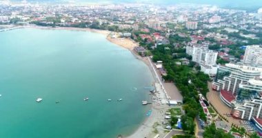 Gelendzhik tatil köyünün merkez plajı kuş bakışı manzaralı. Sıralar dolusu güneş şezlongları ve kumdaki şemsiyeler. İnsanlar yüzer ve güneşlenir. Zümrüt suyu. Sahil boyunca bir kiriş seti var.