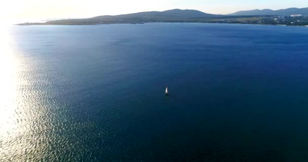 A yacht under sail sails in the turquoise sea. The setting sun casts a long shadow on the water from the sail — Stock Video