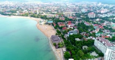 Gelendzhik tatil köyünün merkez plajı kuş bakışı manzaralı. Sıralar dolusu güneş şezlongları ve kumdaki şemsiyeler. İnsanlar yüzer ve güneşlenir. Zümrüt suyu. Sahil boyunca bir kiriş seti var.