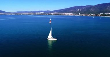 Gelendzhik Körfezi boyunca beyaz yelkenli altında büyük beyaz bir yat, dağlar, Gelendzhik tatil köyü, evler ve plajlara karşı. Dağ olan büyük bir su kütlesi.