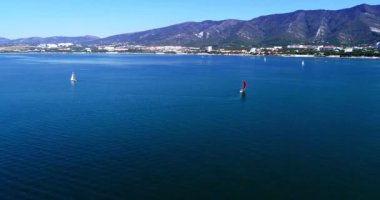 Gelendzhik Körfezi boyunca birkaç güzel beyaz yat, dağların arka planı, Gelendzhik tatil beldesi, evler ve plajlara karşı yelken açıyor. Arkasında dağ olan büyük bir su kütlesi.