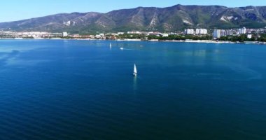 Gelendzhik Körfezi boyunca birkaç güzel beyaz yat, dağların arka planı, Gelendzhik tatil beldesi, evler ve plajlara karşı yelken açıyor. Arkasında dağ olan büyük bir su kütlesi.