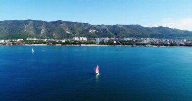 Kırmızı yelkenli altında güzel büyük beyaz bir yat Gelendzhik Körfezi boyunca Gelendzhik tatil beldesinin arka planına doğru yavaşça yelken açar. Büyük bir su kütlesi.