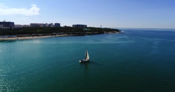 Un gran yate blanco hermoso bajo una vela blanca navega a lo largo de la bahía de Gelendzhik contra el fondo de las montañas, complejo Gelendzhik, casas y playas. Un gran cuerpo de agua con una montaña en el — Vídeos de Stock