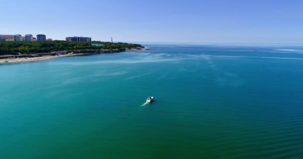 Лодка удовольствия медленно плывет вдоль Геленджикского залива на фоне гор, маяка. Знак над водоемом — стоковое видео