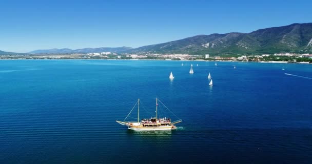 Un barco de madera Pleasure navega a lo largo de la bahía de Gelendzhik en el contexto de las montañas del Cáucaso. Un pequeño barco en un gran cuerpo de agua — Vídeo de stock