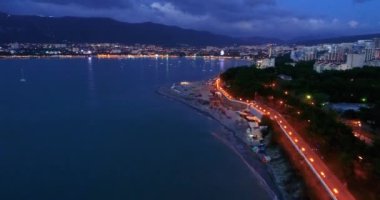 Gelendzhik Tatil Köyü. Akşam alacakaranlıkta tatil köyünün üzerinde uçuyor. Seddin ışıkları, evler, karanlık deniz, sahildeki ışıklar. Arkasında bir şehir olan büyük bir su kütlesi.
