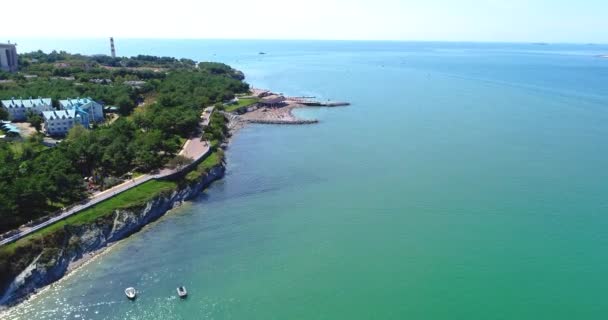 Gelendzhik üdülőhelye. Madártávlatból repül a part felett. Kavicsos strand, napernyők és napozóágyak sora. Az emberek úsznak és napoznak. Felszerelés korláttal. A kilátás a nagy — Stock videók