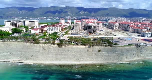 Karadeniz kıyısı boyunca İHA uçuşu. Yüksek kayalık uçurum. Aşağıda bir kiremit plajı şeridi var. Uzakta, Gelendzhik deniz feneri. — Stok video