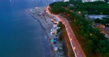 Gelendzhik Tatil Köyü. Akşam alacakaranlıkta tatil köyünün üzerinde uçuyor. Seddin ışıkları, evler, karanlık deniz, sahildeki ışıklar. Arkasında bir şehir olan büyük bir su kütlesi.