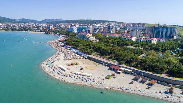 Beach of Gelendzhik resort. Numerous sun umbrellas and sun loungers. Embankment with balustrade. Houses and trees behind the embankment — Stock Photo, Image