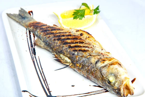 Lubina en la parrilla. Lubina con limón está en un plato blanco cuadrado. Sobre fondo blanco — Foto de Stock