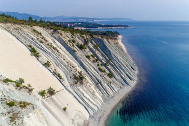 Karadeniz kıyısında Gelendzhik yakınlarında. Çam ağaçlarıyla kaplı yüksek katmanlı kayalar. Kayalıkların dibinde çakıl taşı plajı. Arka planda Gelendzhik ve Kafkasya dağları