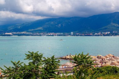 Güneşli bir havada Gelendzhik tatil köyü plajı. Arka planda, Gelendzhik şehri, Körfez ve Kafkasya dağları.