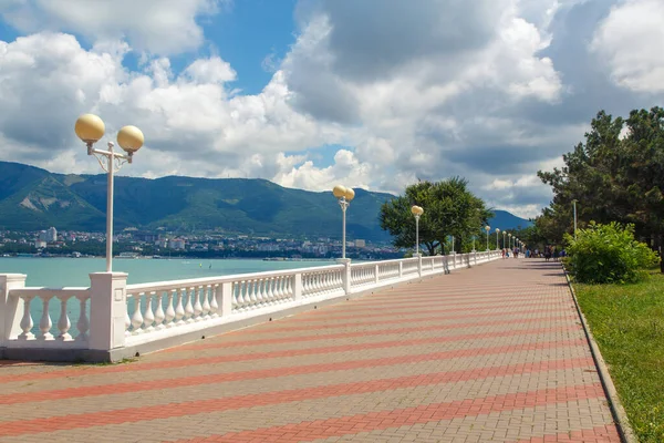 El terraplén del balneario de Gelendzhik en tiempo soleado claro. Balaustrada blanca y farolas. Al fondo, la bahía de Gelendzhik y las montañas del Cáucaso . — Foto de Stock