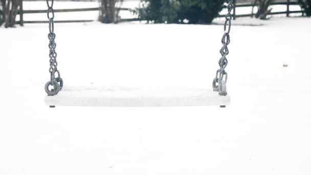 Empty swing moving slowly with snow on it in the winter season — Stock Video