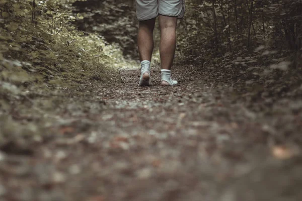 Männliche Füße laufen mit zerrissenen Socken durch einen grünen Wald — Stockfoto