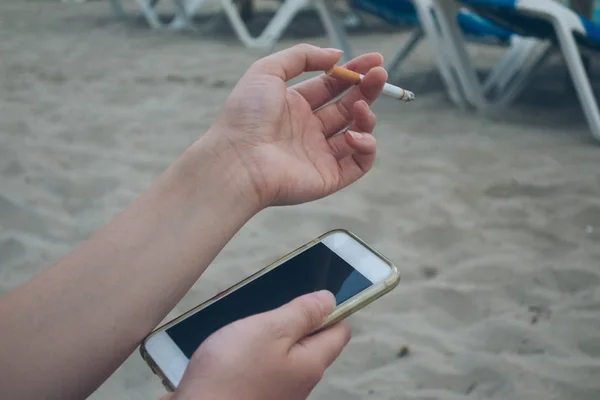 Kvinnan på stranden håller en smartphone och en cigg i den andra handen — Stockfoto