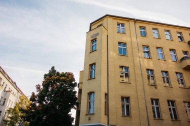 Turuncu köşeli bina, sokağın ortasında sonbahar ağacı var.