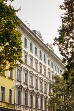 Yeşil ağaçlar tarafından çerçevelenmiş tarihi ve lüks bir ev cephesi.