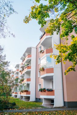 Beyaz balkonu ve yanında yeşil sonbahar yaprakları olan gül renkli bir ev.