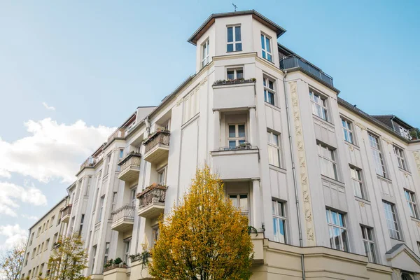 Önünde sarı ağaç olan büyük, beyaz bir bina.