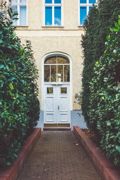 white wooden entrance door framed by green bushes