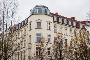Corner hexagonal tower on a classic urban apartment block amongst bare autumn trees in a low angle view under a grey cloudy sky