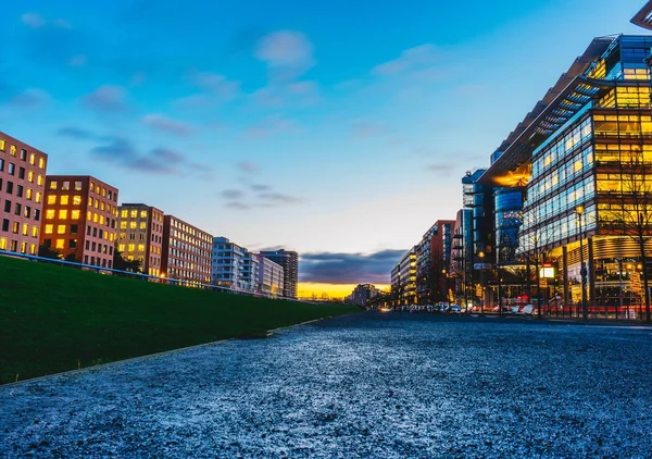 Low angle view of a downtown CBD at sunset with rows of office blocks and apartments lining a street with illuminated windows and a pink glow in the sky