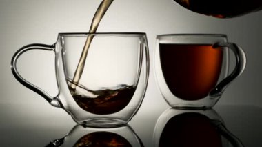 Siyah çay, beyaz arka planda cam bir fincana dökülür.