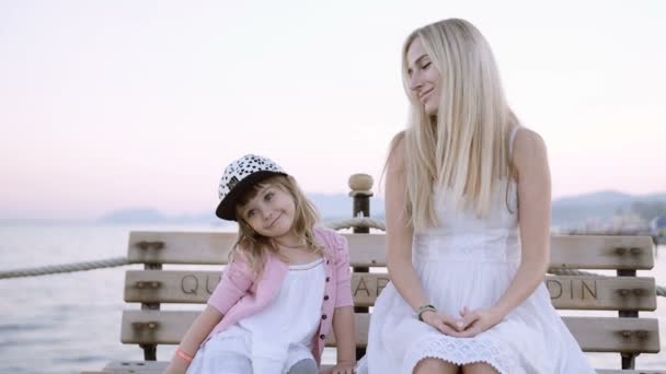 Mamá y su hija están sentadas en el banco de la playa en el muelle — Vídeos de Stock