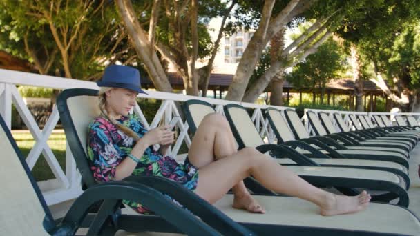 Mladá žena používající mobil vleže na lehátko v hotelu — Stock video