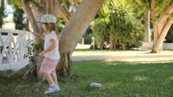 Милая маленькая девочка собирает палки деревьев с травы и прыгает — стоковое видео