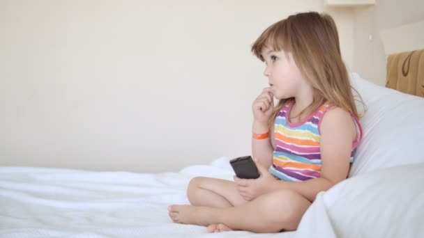 Adorable child in colourful dress watching tv on the bed — Stock Video