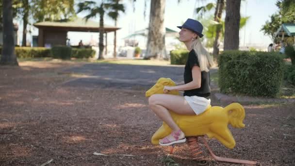 Jovem bela mulher montar brinquedo cavalo em um parque infantil — Vídeo de Stock