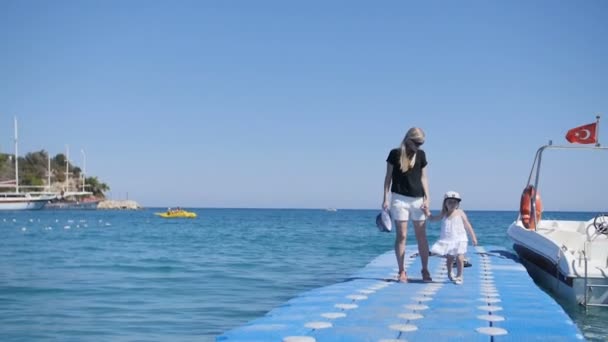 Mother and girl walks on pier, swing by waves. — Stock Video