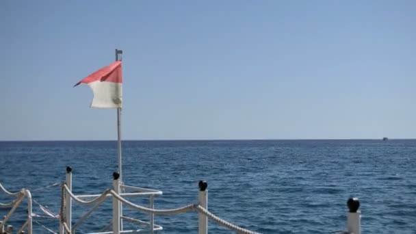 Pier mit einer Rettungsschwimmerfahne, die in einer leichten Brise des Mittelmeeres flattert — Stockvideo