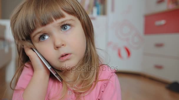 Criança pequena, como um adulto, falando em um smartphone enquanto sentada em um tapete em seu quarto — Vídeo de Stock