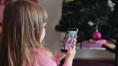 aile ev oturma odasında şenlikli ışıkları ile güzel Noel ağacı küçük kız almak fotoğraf bir mobil telefon