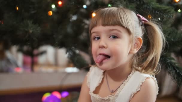 Happy Baby meisje grimas Shes gezicht. Kerstboom op achtergrond — Stockvideo