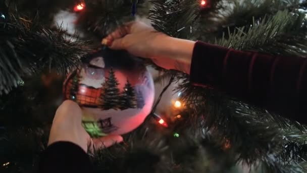 Close up de belas mãos jovens decorar a árvore de Natal com grande bola — Vídeo de Stock