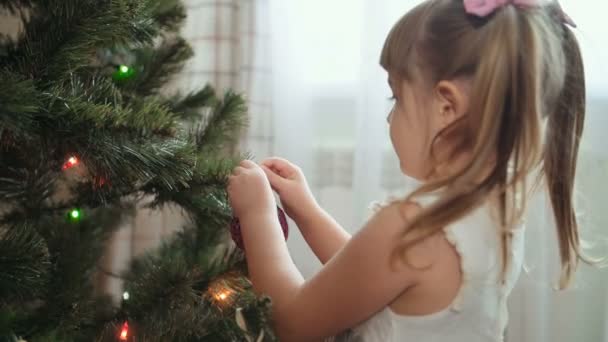 Schattig klein meisje versiert de kerstboom. — Stockvideo