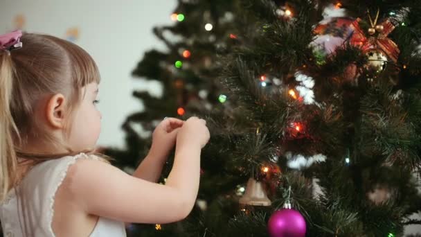 Schattig klein meisje versiert de kerstboom. — Stockvideo