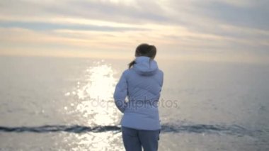 Uzun saçlı güzel sarışın kadın denize batarken yürür.